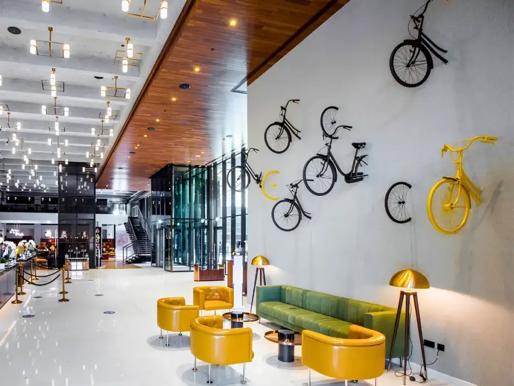 Modern hotel lobby with yellow chairs, green sofa, and lamps. Decorative bicycles mounted on a white wall as art, curated by interioritalia art consultant in Dubai. Bright, open space with wood and glass details.