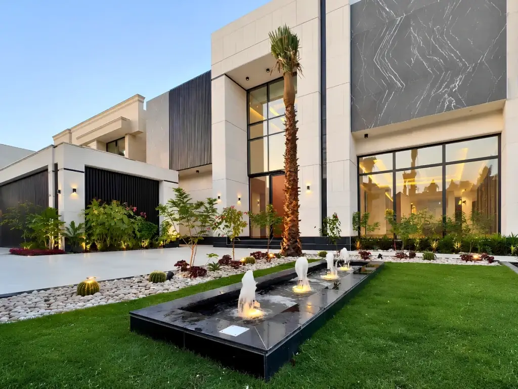 Modern house exterior with large windows and marble accents. A sleek fountain and lush landscaping with palm trees create a luxurious atmosphere.