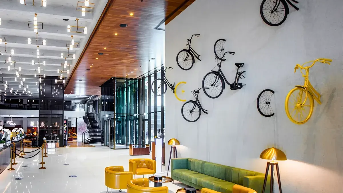 Modern hotel lobby with yellow chairs, green sofa, and lamps. Decorative bicycles mounted on a white wall as art, curated by interioritalia art consultant in Dubai. Bright, open space with wood and glass details.