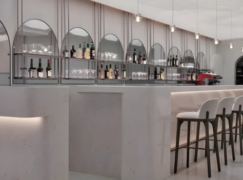 Modern bar interior with a curved counter, high stools, and a back wall displaying bottles and glassware under arched mirrors, with pendant lights hanging from the ceiling.